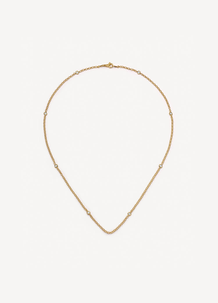 A delicate yellow gold chain necklace with evenly spaced diamond details, displayed on a clean, light off-white background.
