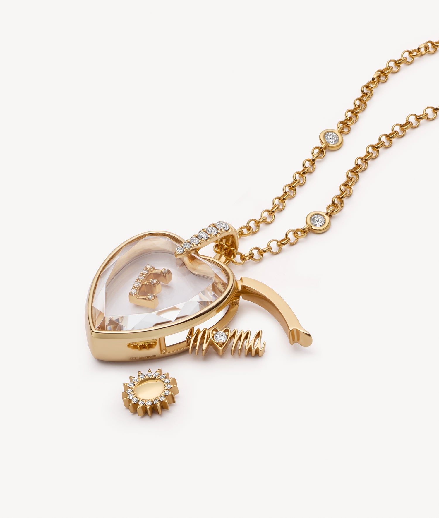 Gold heart-shaped locket necklace with a clear crystal face, shown open with a small gold letter 'E' charm inside, alongside a sun and a mama charm.