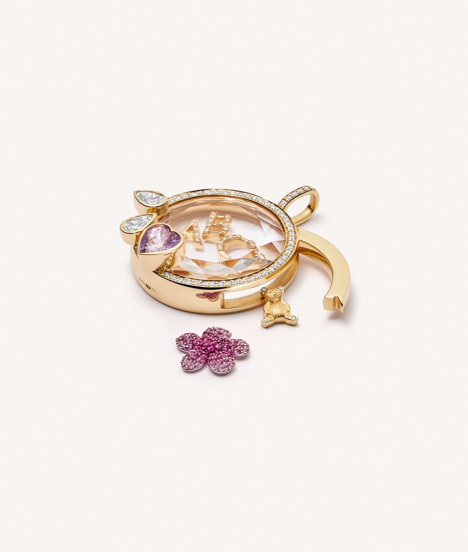 Blooming blossom charm outside an open round yellow gold locket set with a pink sapphire heart.