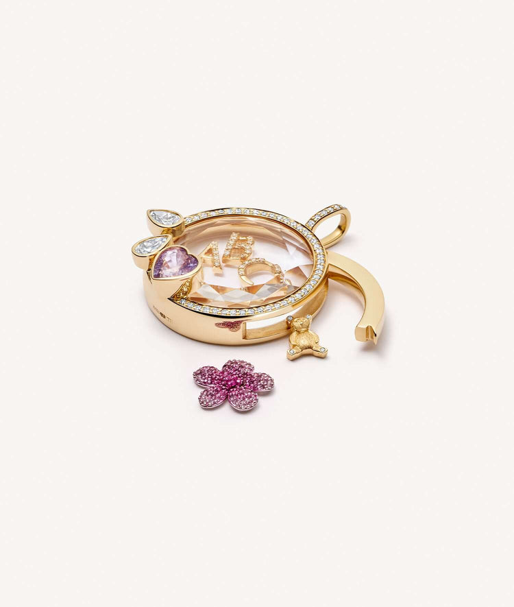 Blooming blossom charm outside an open round yellow gold locket set with a pink sapphire heart.