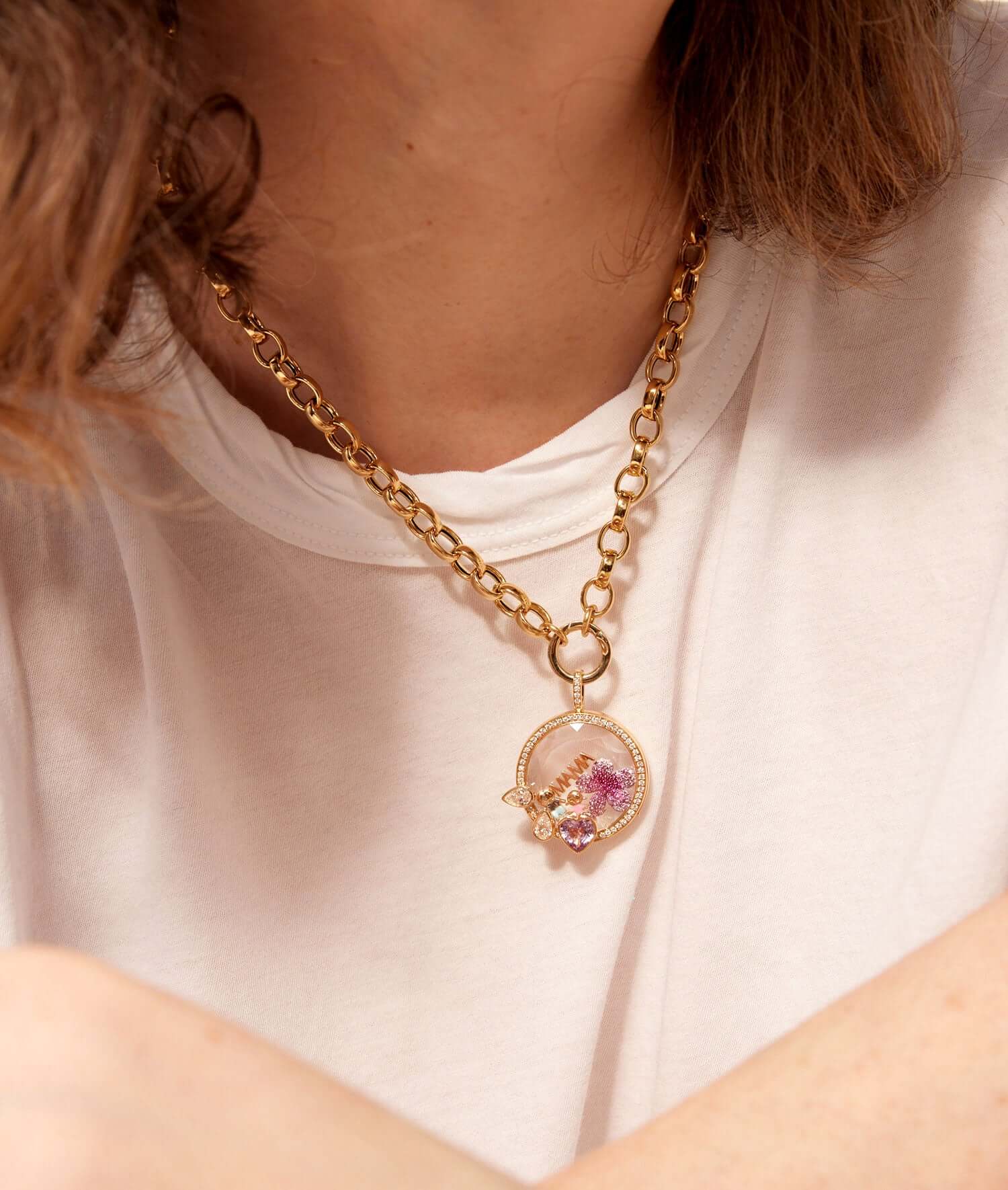 Aphrodite round yellow gold, diamond and sapphire locket with diamond bell and charms styled on a model wearing a white tee shirt.