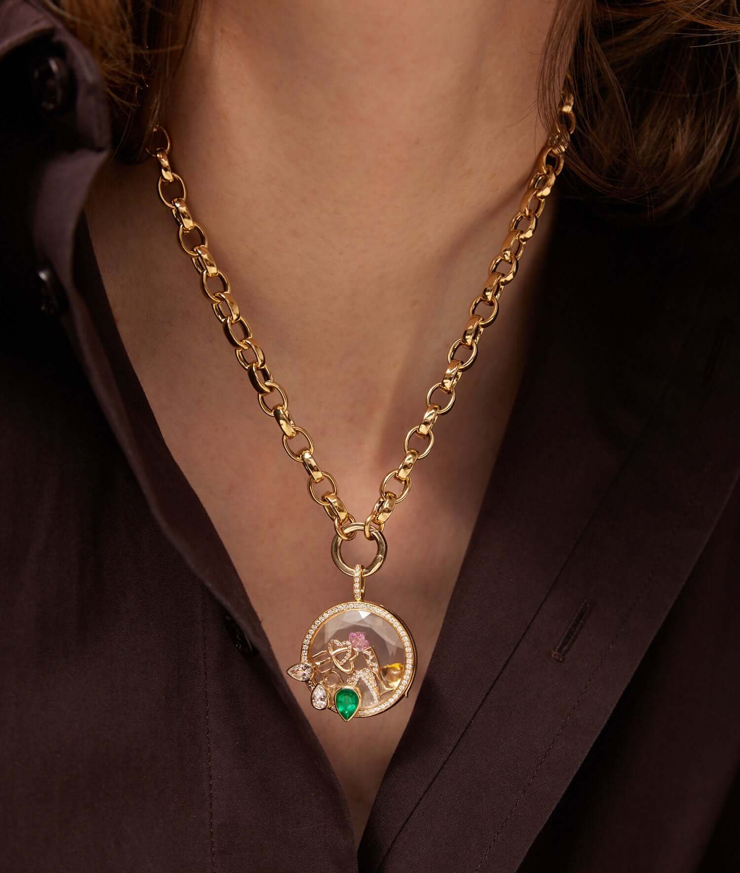 Athena Emerald Pear drop locket styled with charms against a brown silk shirt.