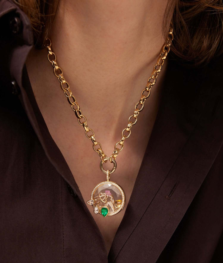 Athena Emerald Pear drop locket styled with charms against a brown silk shirt.
