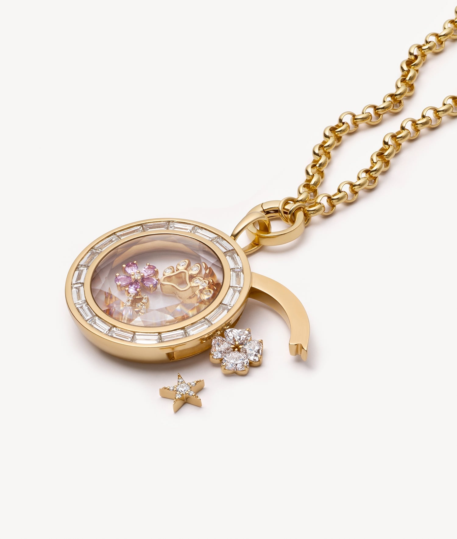 A gold locket necklace with a clear crystal facade containing pink and gold charm, shown with a matching gold chain and small dangling charms outside the locket pendant on a light off-white background.
