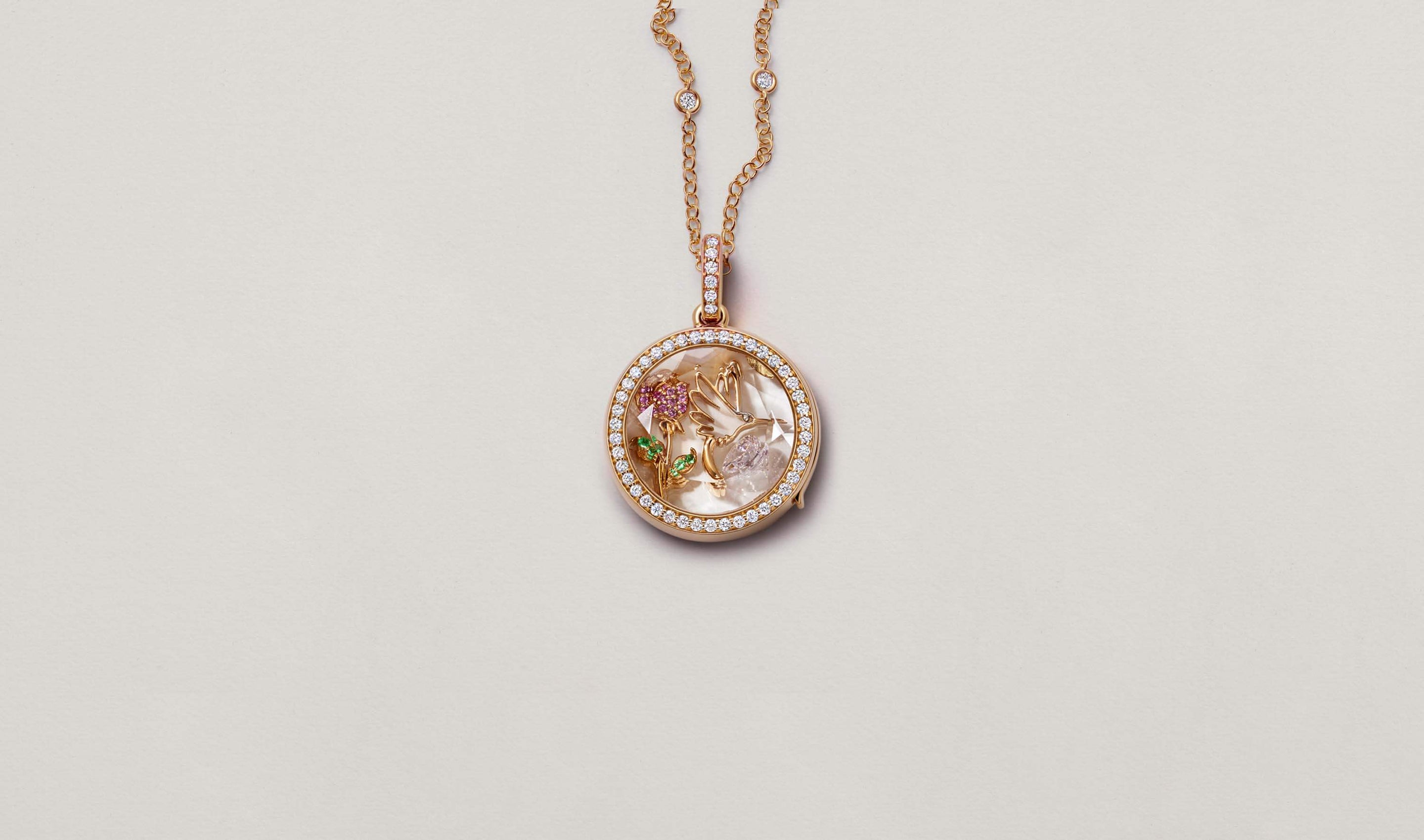 Helios Round Diamond Rose Gold Locket 18k on a rose gold diamond chain with a Pink Sapphire Rose Charm, Hummingbird Spirit Animal Charm and April Birthstone Charm photographed on a neutral background.
