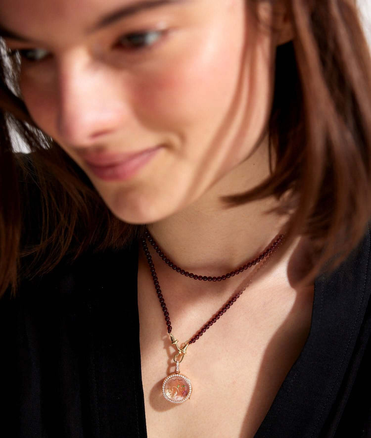 helios round diamond, rose gold locket with rose charm  with a garnet beaded chain, styled on a model with a black shirt.
