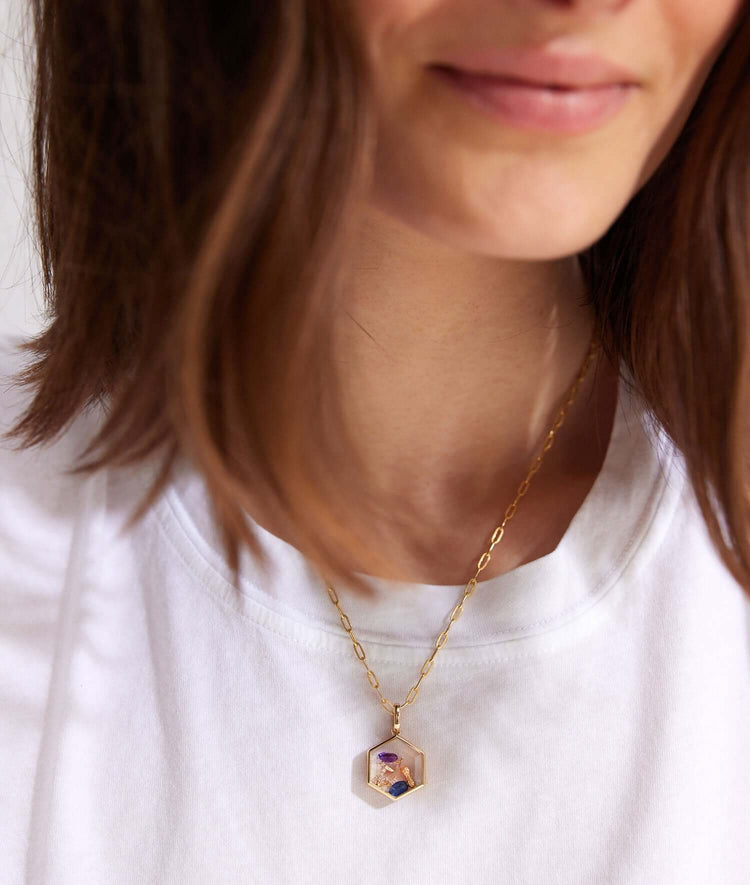 Yellow gold honeycomb locket styled with charms, on model with a white tee shirt.