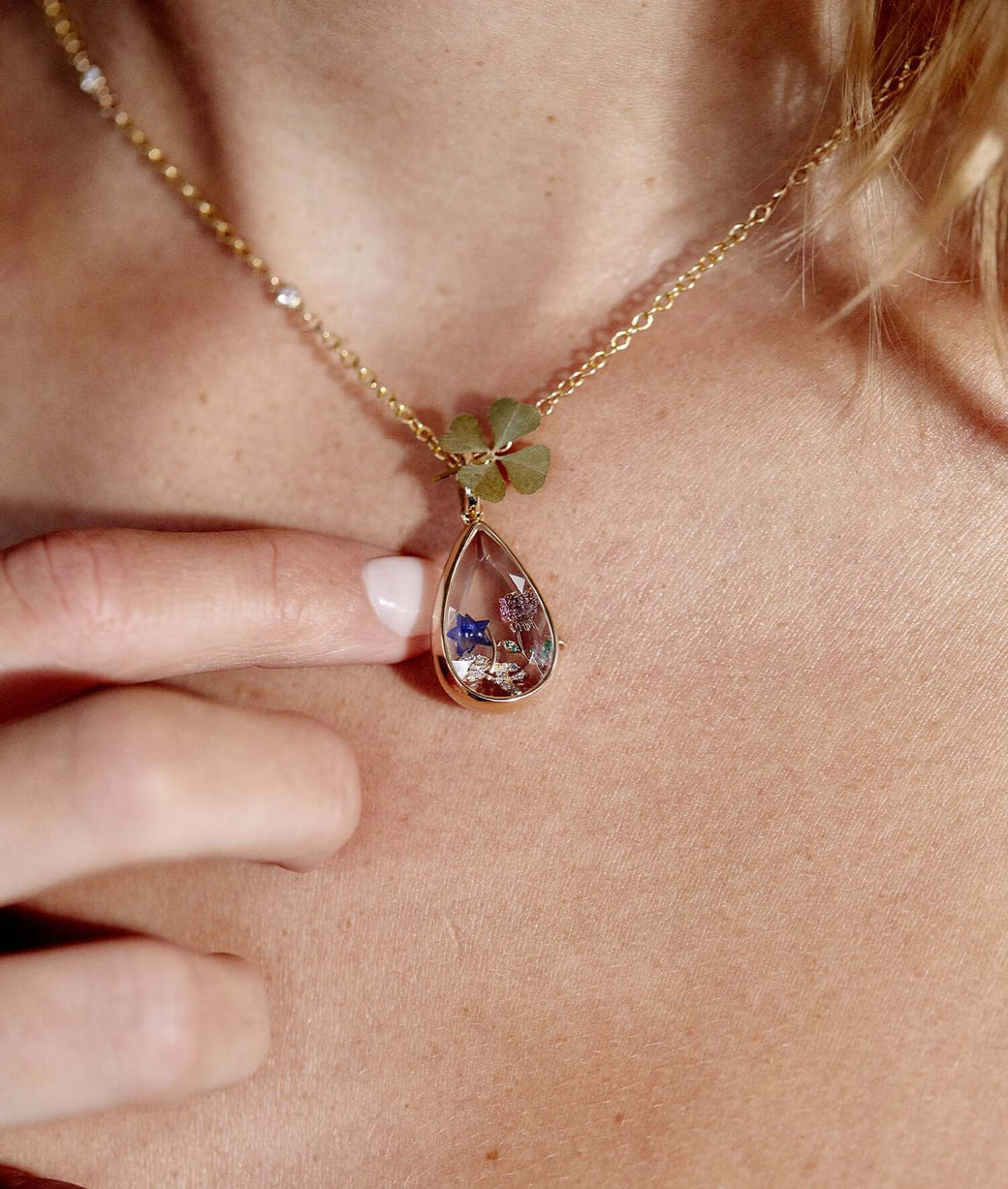 Lacrima teardrop gold locket with charms, styled on a model with a real four leaf clover. 