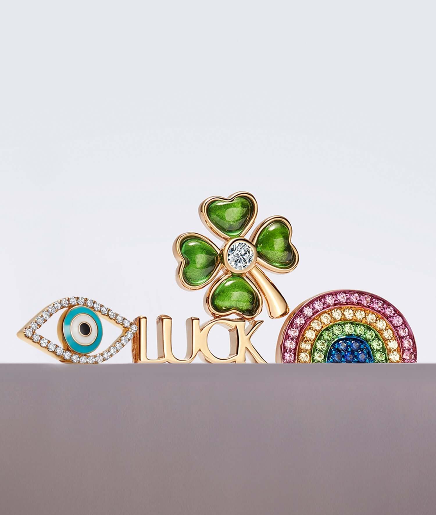 Stack of luck charms including an diamond evil eye, yellow gold luck script word, four leaf clover and a sapphire rainbow yellow gold charms