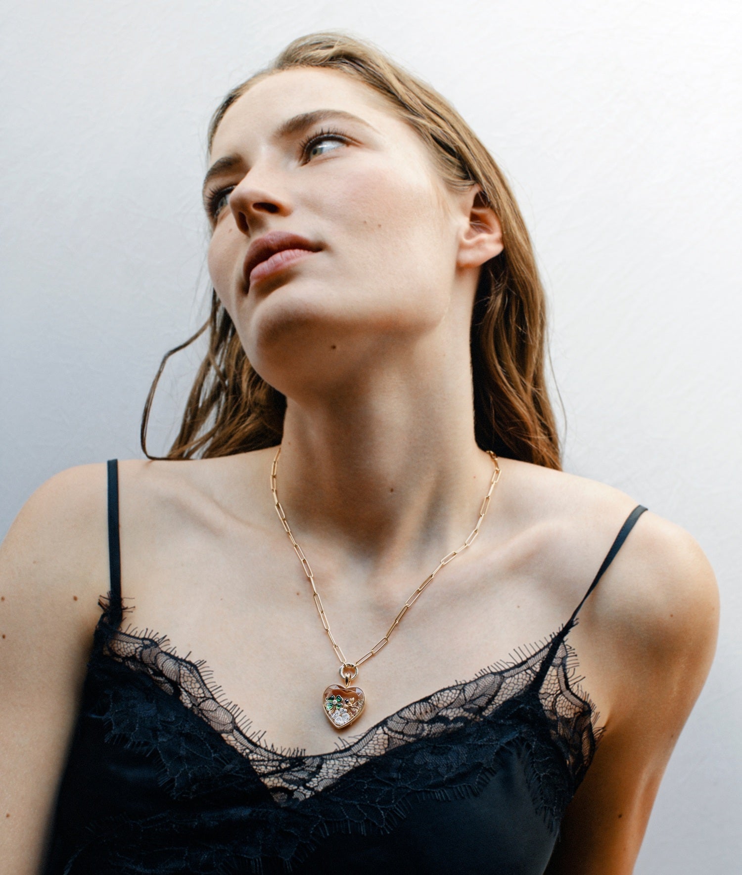 Model wearing a large heart locket pendant on a yellow gold chain with a black lace top