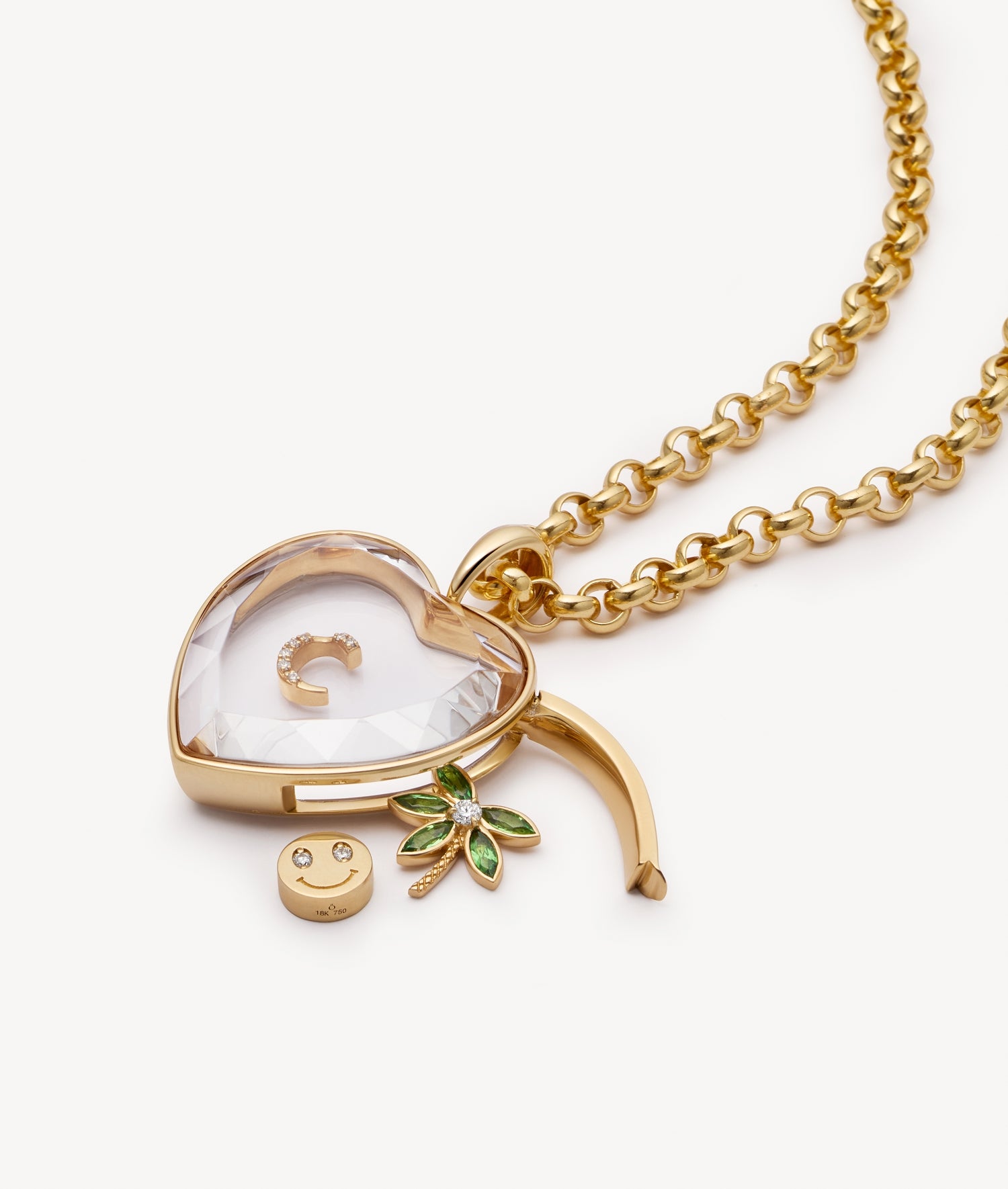 Gold heart-shaped pendant necklace with a crystal faceted, a gold smiley face charm, and a green leaf accent, shown on a white background.