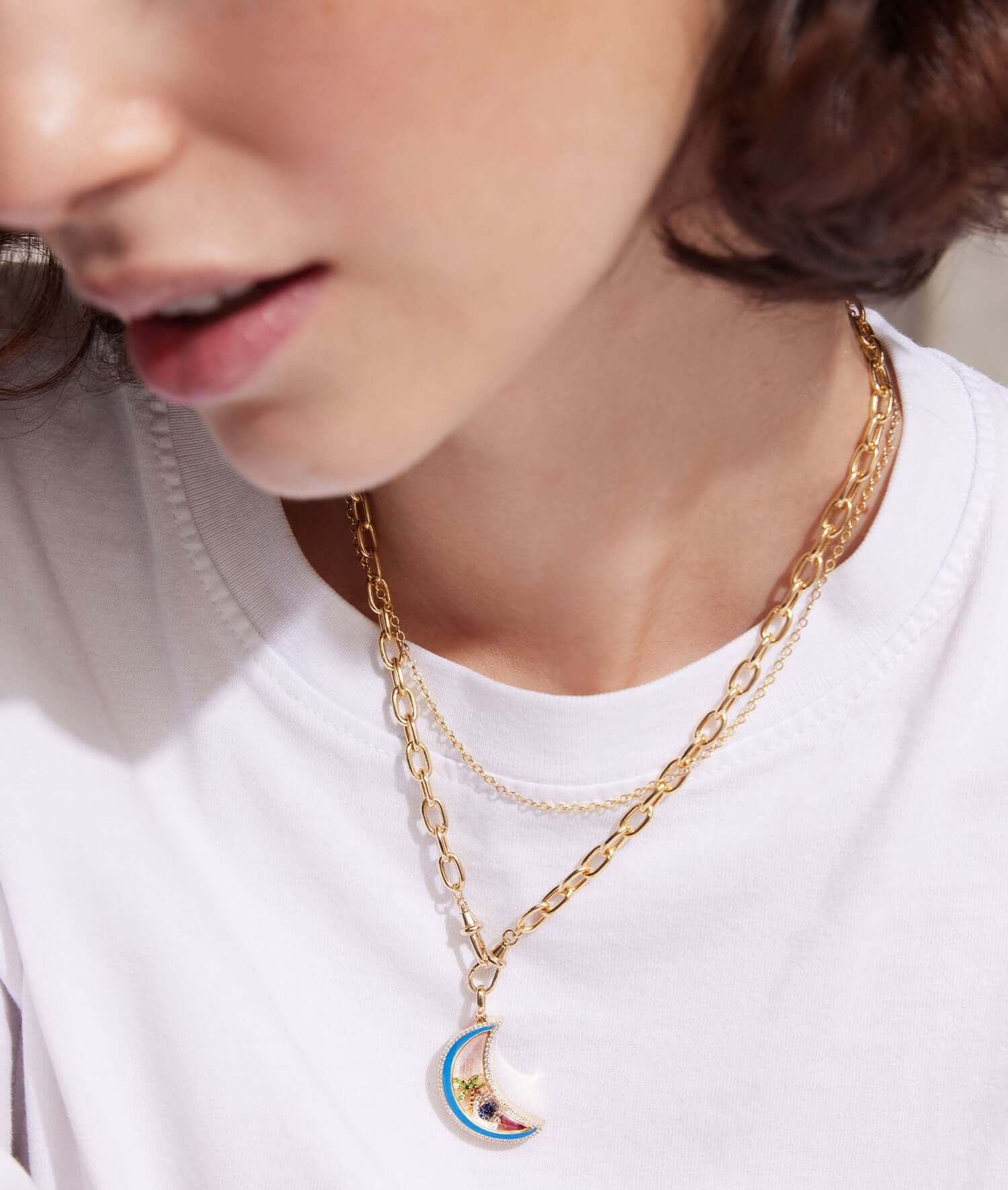 Lunar crescent moon diamond locket styled with charms on a paperclip chain on a model in a white tee shirt.