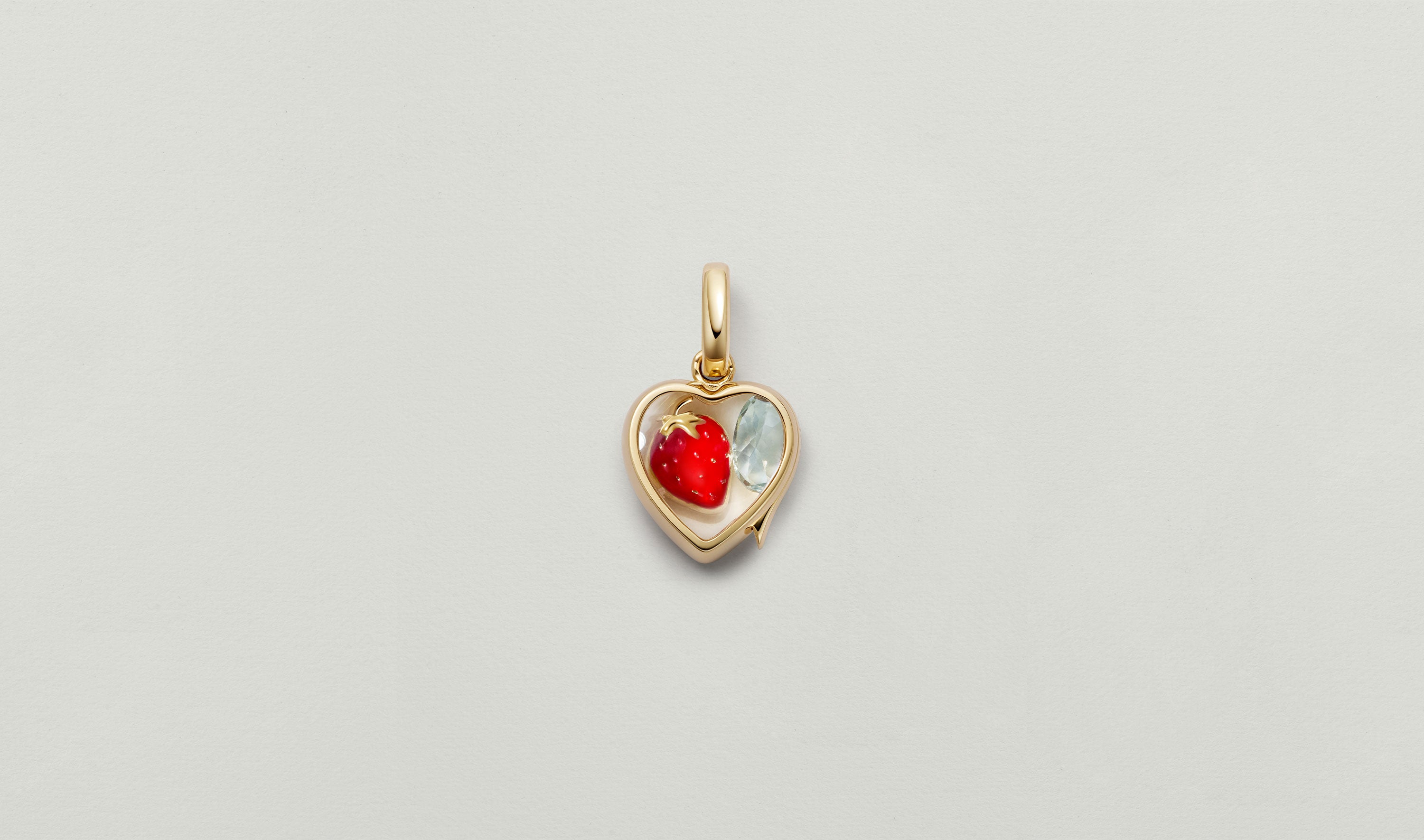 mini heart of gold locket styled closed with a strawberry charm and an aquamarine charm.
