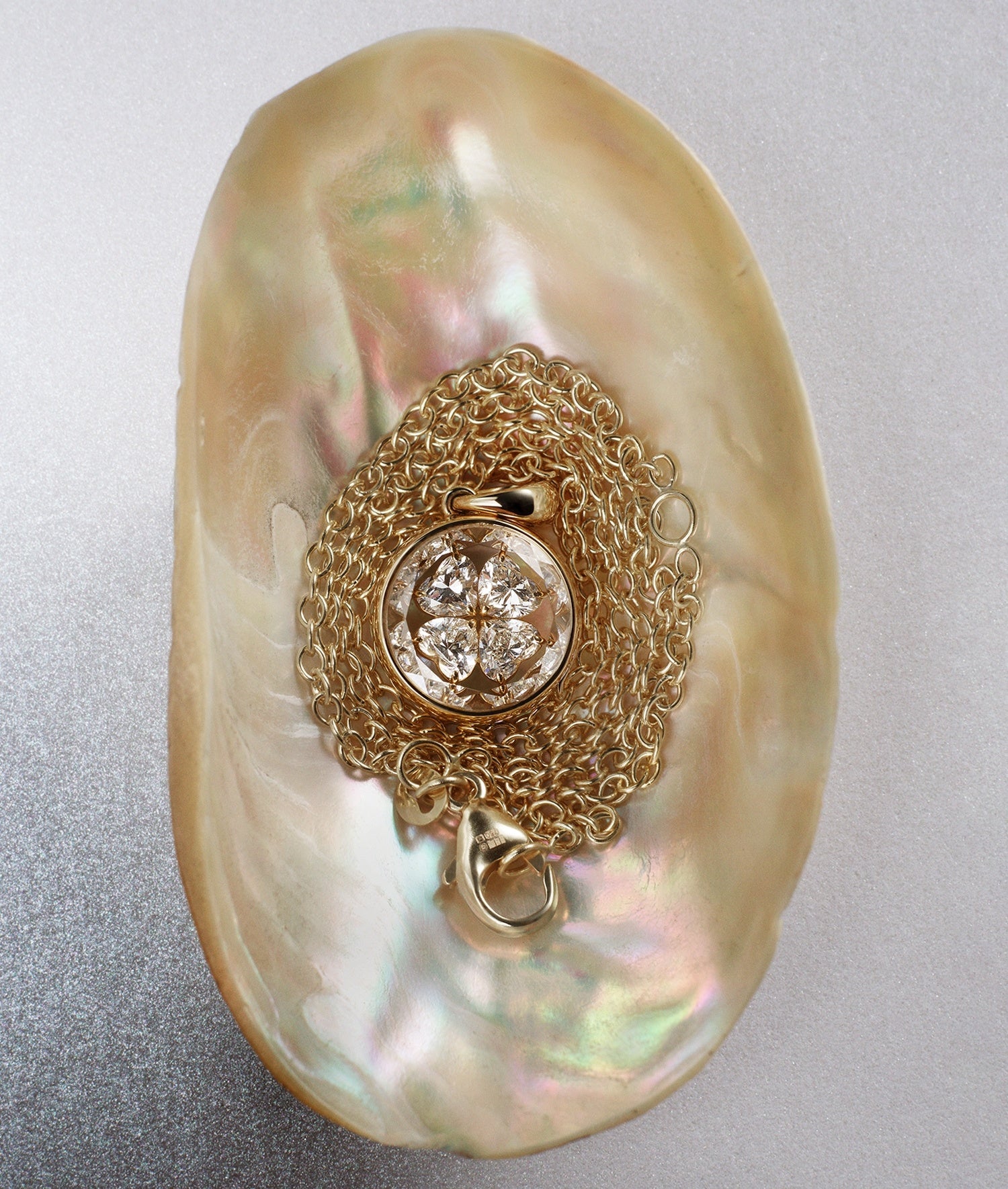 Mini round locket pendant on a rolo yellow gold chain styled with a diamond clover charm inside a nacre shell