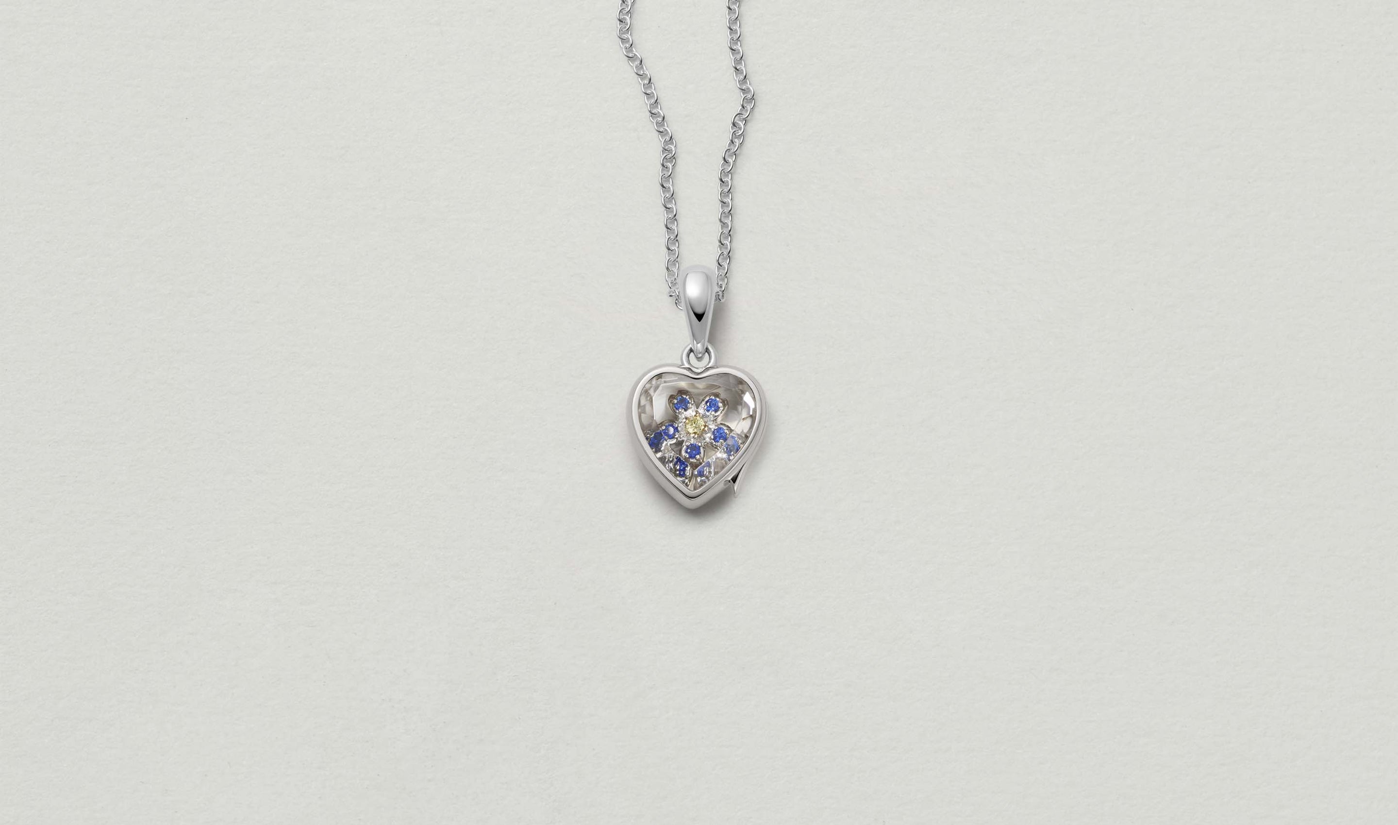 Mini White Heart of Gold Locket 14k personalised with colourful solid 18k gold charms and hanging on a white gold chain photographed on a neutral background.