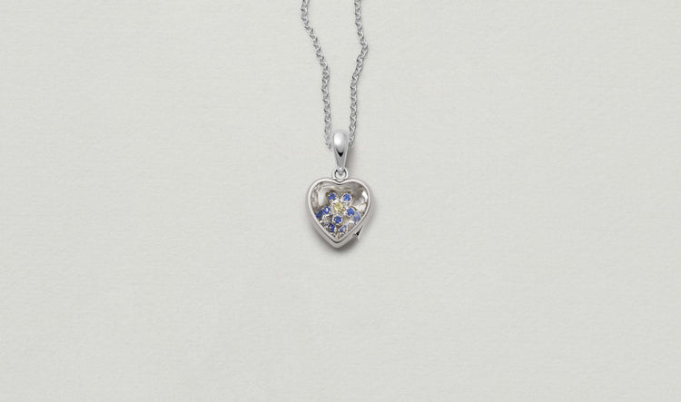 Mini White Heart of Gold Locket 14k personalised with colourful solid 18k gold charms and hanging on a white gold chain photographed on a neutral background.