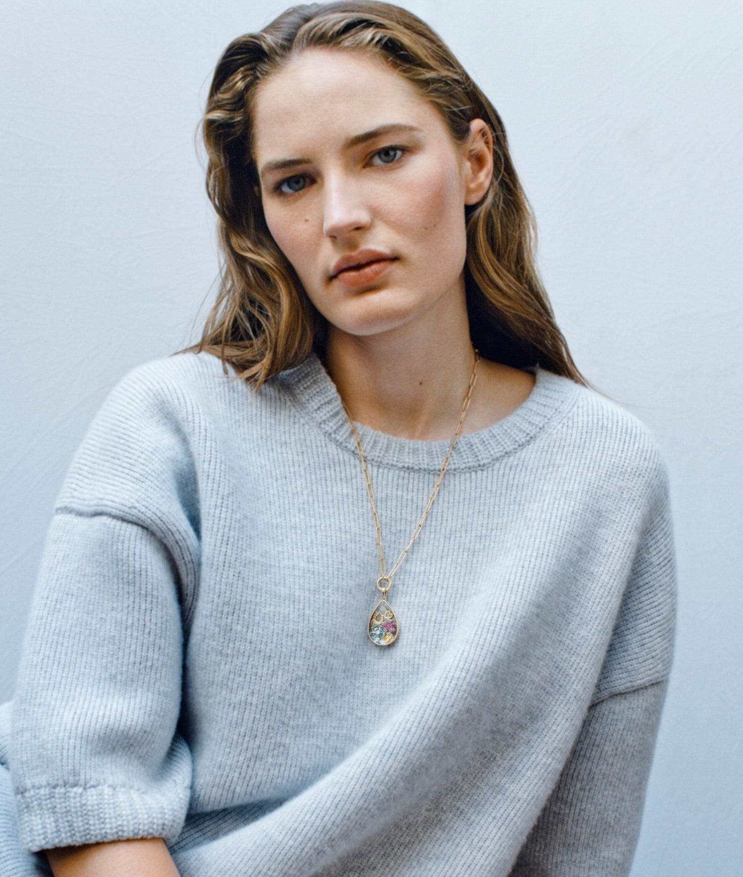 Model wearing a blue jumper with a teardrop crystal facade locket pendant styled with diamond charms
