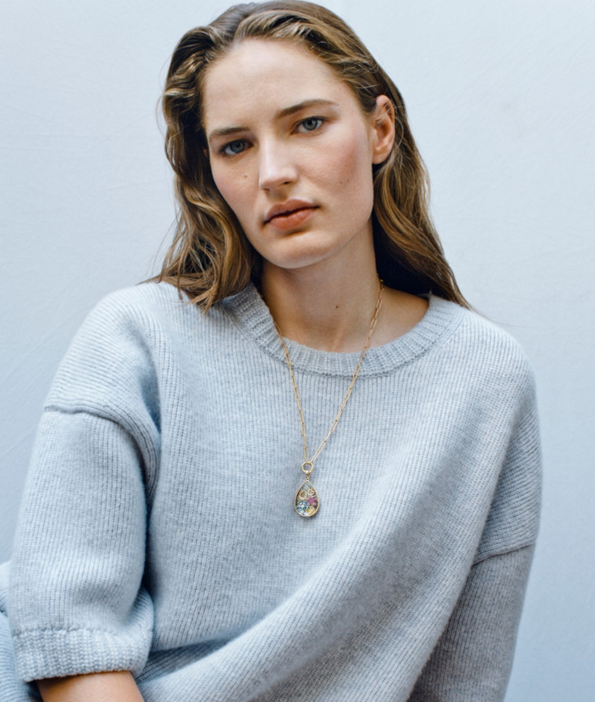 Model wearing a blue jumper with a teardrop crystal facade locket pendant styled with diamond charms
