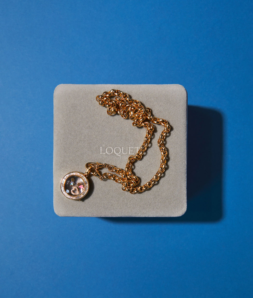 diamond round gold locket with charms on a loquet box with a blue background.