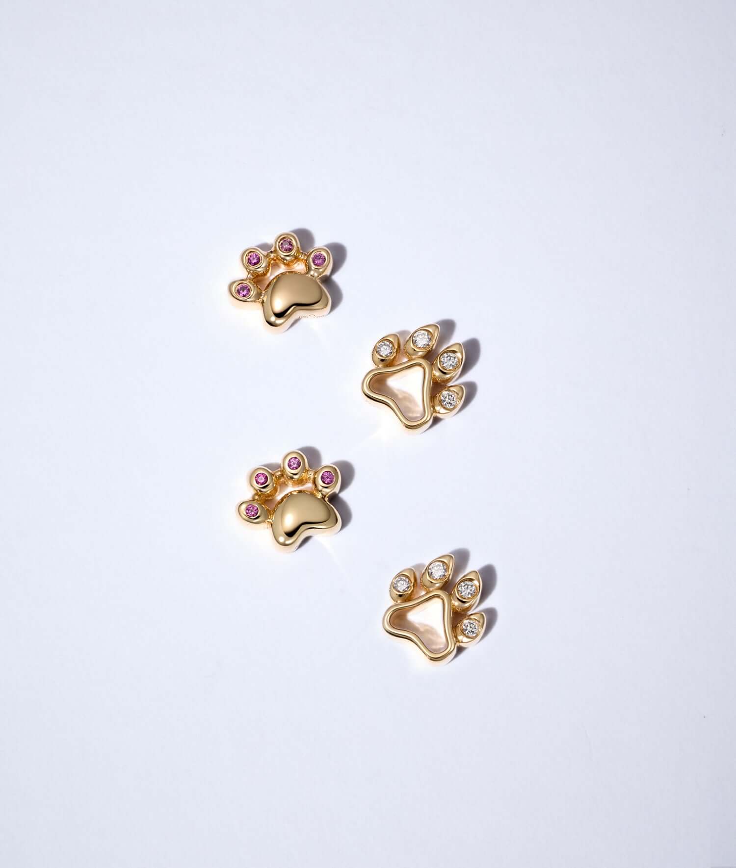 two cat paw charms and two dog paw charms in yellow gold set with pink sapphires and diamonds.