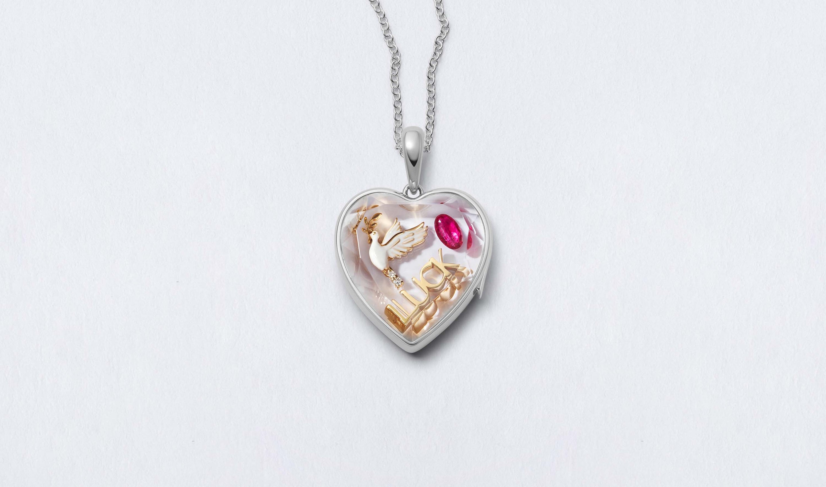 White Heart of Gold Locket 14k personalised with colourful solid 18k gold charms and hanging on a white gold chain photographed on a neutral background.