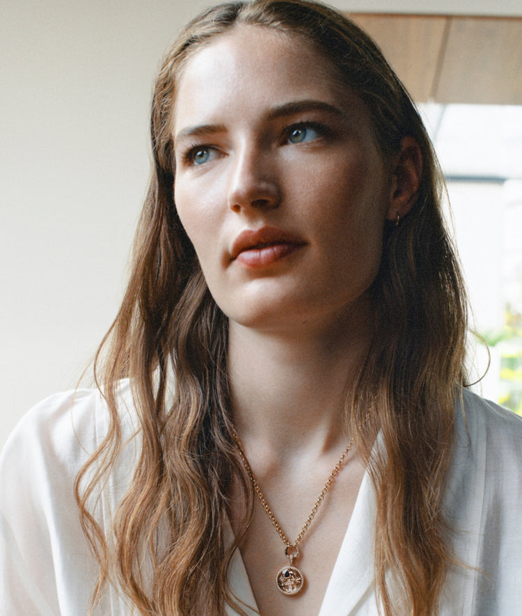 Portrait of a model wearing a diamond round locket pendant on a chain styled with charms with a white top shirt